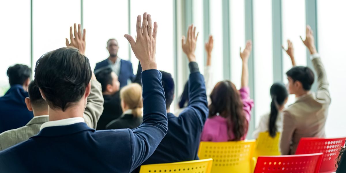 pessoas com braço levantado durante uma assembleia de consorcio